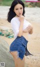 A woman in a white shirt and blue shorts posing on a beach.