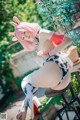 A woman with pink hair sitting on a stool.