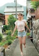 A woman walking down a street in a pink shirt and denim shorts.