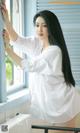 A woman in a white shirt leaning against a window.