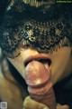 A woman in a black lace mask is sucking a large dildo.