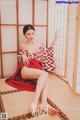 A woman in a red and white kimono sitting on a tatami mat.