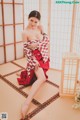 A woman in a red and white kimono sitting on a tatami mat.