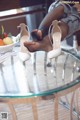 A woman sitting on top of a glass table next to a bowl of fruit.
