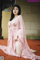 A woman in a pink robe sitting on a red carpet.