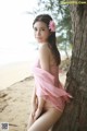 A woman in a pink dress leaning against a tree on the beach.
