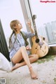 A woman sitting on the floor with a guitar and a glass of water.