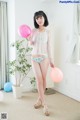 A woman in a white blouse and blue panties holding pink balloons.