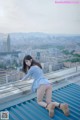 A woman in a blue dress is sitting on a roof.