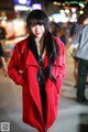 A woman in a red coat is standing in the street.