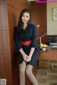 A woman in a blue dress sitting on a desk.