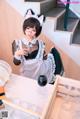 A woman dressed as a maid sitting at a table with a glass of wine.