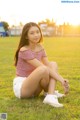 A woman sitting on the grass in a field at sunset.