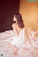 A woman sitting on a bed in a white dress.