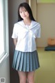 A woman in a school uniform standing by a window.